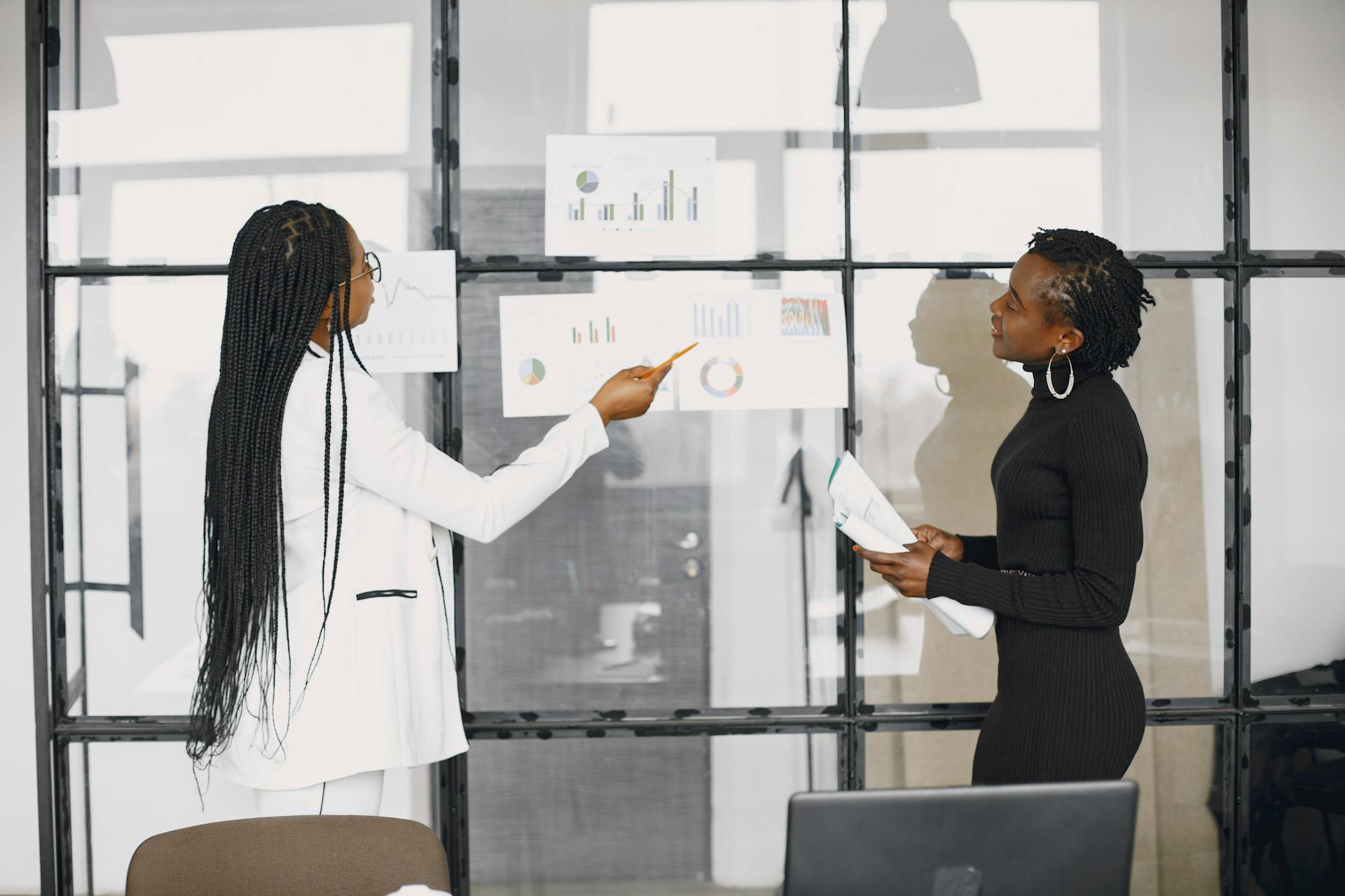 Two African women in colorful prints collaborating on a laptop in a library